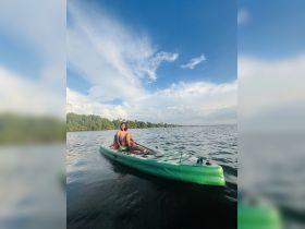 A person enjoys kayaking on calm waters, surrounded by lush greenery and a beautiful sky — a perfect snapshot of outdoor adventure.