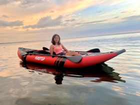 A young woman enjoys a serene kayaking experience at sunset, surrounded by calm waters and beautiful skies — perfect for adventure seekers and nature lovers.
