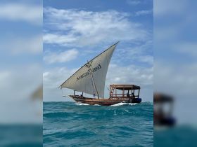 A traditional sailboat, named 'Karibu Zanzibar', gracefully navigates through the turquoise waters, showcasing the beauty of maritime adventures.