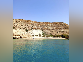 A serene view of a beach with clear turquoise waters, featuring a person kayaking and a boat in the distance — perfect for showcasing beautiful coastal destinations.
