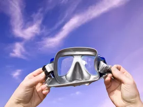 A close-up of a snorkel mask held against a vibrant blue sky, perfect for underwater adventures and exploring marine life.