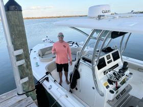 A man stands at the helm of a well-equipped boat, showcasing the modern console and seating area — perfect for a day on the water.