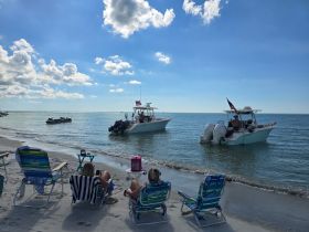 Guests relax on the beach while boats approach the shore, creating a perfect setting for a day of fun and water activities.