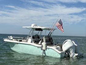 A pristine center console boat anchored in calm waters, showcasing its sleek design and American flag — perfect for fishing or leisurely outings.