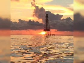 A stunning sunset casts vibrant colors over the water, with a lighthouse silhouette creating a picturesque scene — perfect for capturing the beauty of coastal landscapes.