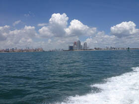 A stunning view of the city skyline against a backdrop of fluffy clouds and shimmering waters, perfect for showcasing the beauty of a boat trip.