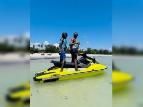 Two friends pose on a vibrant yellow jet ski at the beach, ready for an exciting day of water sports and adventure.