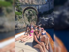 A joyful group of friends relaxes on a boat, soaking up the sun and enjoying their time together against a stunning coastal backdrop.