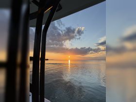 A stunning sunset view from the deck of a boat, showcasing the tranquil waters and vibrant sky — perfect for evening cruises.