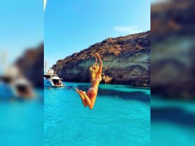 A woman joyfully leaps into the crystal-clear waters from a boat, capturing the essence of summer fun and adventure on the water.