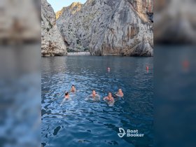 A lively group enjoys a refreshing swim in a stunning rocky cove, surrounded by dramatic cliffs and clear waters — perfect for adventurous outings.