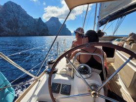 A couple enjoys a scenic sailing experience with stunning rock formations in the background, perfect for romantic getaways on the water.