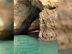 A stunning view of a natural cave along the coastline, with visitors enjoying the beach inside — a perfect spot for exploration and adventure.