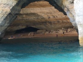 A stunning view of a beach inside a cave, with groups of people kayaking and enjoying the serene waters — a perfect destination for adventure seekers.