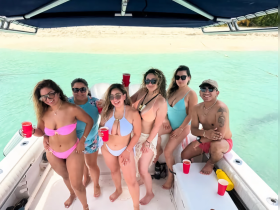 A lively group of friends enjoys a fun day on the boat, celebrating with drinks and laughter in the beautiful turquoise waters.