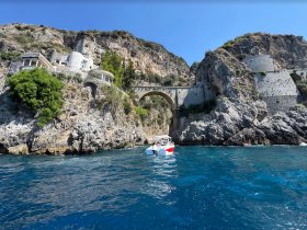 A picturesque view of a small boat navigating along a stunning rocky coastline, showcasing the beautiful architecture and natural landscape of the area.