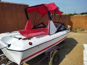 A sleek speedboat with a vibrant red canopy and seating, showcased on a trailer — perfect for water adventures and leisure outings.
