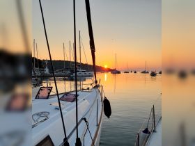 A stunning sunset view from the deck of a yacht, showcasing a tranquil marina filled with boats — perfect for evening cruises and relaxation.
