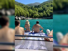 A group enjoys a relaxing day on a boat, soaking in the stunning scenery of turquoise waters and lush greenery — perfect for summer adventures.