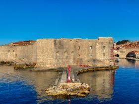 A scenic view of a historic stone fortification by the water, showcasing the architectural beauty and surrounding landscape.