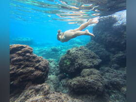 A child enjoys snorkeling in crystal-clear waters, exploring vibrant underwater rock formations — a perfect adventure for young explorers.