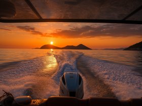 A stunning sunset view from the back of a boat, showcasing the tranquil waters and distant islands — perfect for evening cruises.