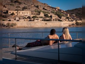 A couple relaxes on the deck of a boat, enjoying the scenic view of historic ruins along the coastline — a perfect moment for romantic getaways or sightseeing tours.