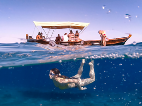 A swimmer explores the vibrant underwater world while a group enjoys their time on a boat above — a perfect snapshot of adventure and fun in the water.