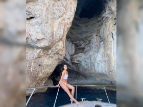 A woman poses on the bow of a boat near a stunning cave, showcasing the beautiful scenery and perfect for a day of exploration and adventure on the water.