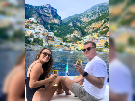 A couple enjoys cocktails on a boat while admiring the stunning Amalfi Coast — a perfect moment for romantic getaways or celebrations on the water.
