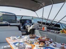 An elegant interior view of a yacht's helm and dining area, beautifully set with a gourmet breakfast spread, showcasing the luxurious experience of dining on the water.
