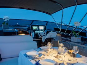 An elegant dining setup inside a luxury boat, featuring a beautifully arranged table with glassware and a view of the helm, perfect for intimate dinners on the water.