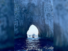 A stunning view of boats passing through a natural archway along the coastline, showcasing the beauty of the ocean and surrounding cliffs.