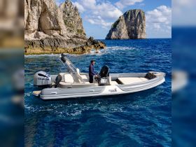 A man navigates a sleek boat through crystal-clear waters near a stunning rocky coastline, showcasing the beauty of ocean adventures.