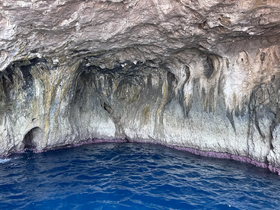An unclear view of a rocky cave structure by the water, showcasing natural formations but lacking clarity and identifiable features.