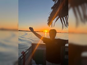 A joyful moment captured as a person celebrates against a stunning sunset backdrop on a boat, showcasing the perfect atmosphere for evening cruises.