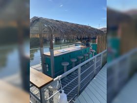 A vibrant outdoor bar area with seating and a thatched roof, perfect for enjoying drinks by the water. Ideal for social gatherings and relaxation.