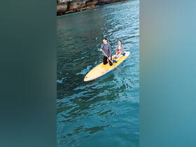 A couple enjoys paddleboarding on tranquil waters, surrounded by stunning cliffs — a perfect adventure for water enthusiasts.