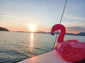 A vibrant pink flamingo float sits on the deck as the sun sets over the tranquil waters, creating a perfect backdrop for relaxation and fun on the water.