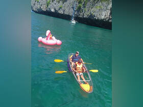 A fun kayaking adventure with a child enjoying a pink flamingo float in crystal-clear waters, surrounded by stunning cliffs — perfect for family outings and water sports.