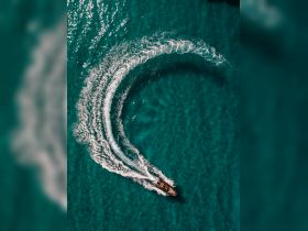 An aerial view of a speedboat making a sharp turn in crystal-clear turquoise waters, showcasing the thrill of boating adventures.