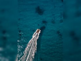 A stunning aerial view of a boat cruising through crystal-clear turquoise waters, showcasing the beauty of the ocean and the vessel's sleek design.