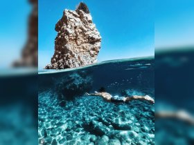 A swimmer glides through crystal-clear waters, showcasing stunning underwater scenery and a rocky outcrop above — an ideal moment for adventure seekers and nature lovers.