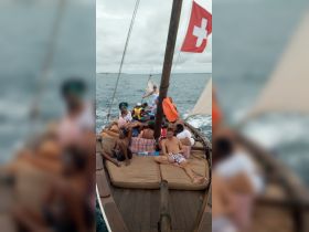 A lively group enjoys a sailing experience on a cozy boat, relaxing on plush seating while taking in the ocean views.