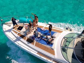 A lively group enjoys a fun day on a yacht, celebrating with drinks and laughter against the backdrop of stunning turquoise waters.