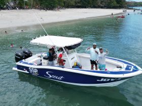 A lively group enjoys a day on the water aboard a Scout boat, with beachgoers in the background and smiles all around — perfect for a fun-filled beach outing.