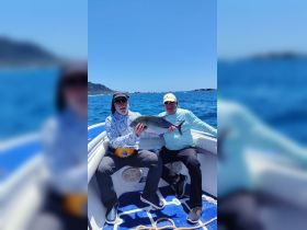 Two friends proudly display their catch while fishing on a boat in the ocean, showcasing the thrill of a successful day on the water.