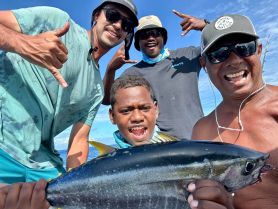 A joyful group of friends celebrates a successful fishing trip, showcasing their catch against a beautiful ocean backdrop.