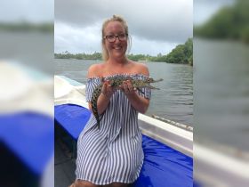 A woman joyfully holds a crocodile while on a boat, showcasing a unique wildlife encounter in a scenic waterway.