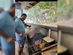 A chef skillfully grills a variety of meats at a scenic outdoor kitchen, perfect for catering memorable boat trips and beach barbecues.